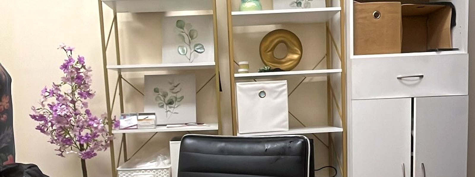 Shelves with eucalyptus prints, a gold ring ornament and a sprig of purple flowers beside a black chair